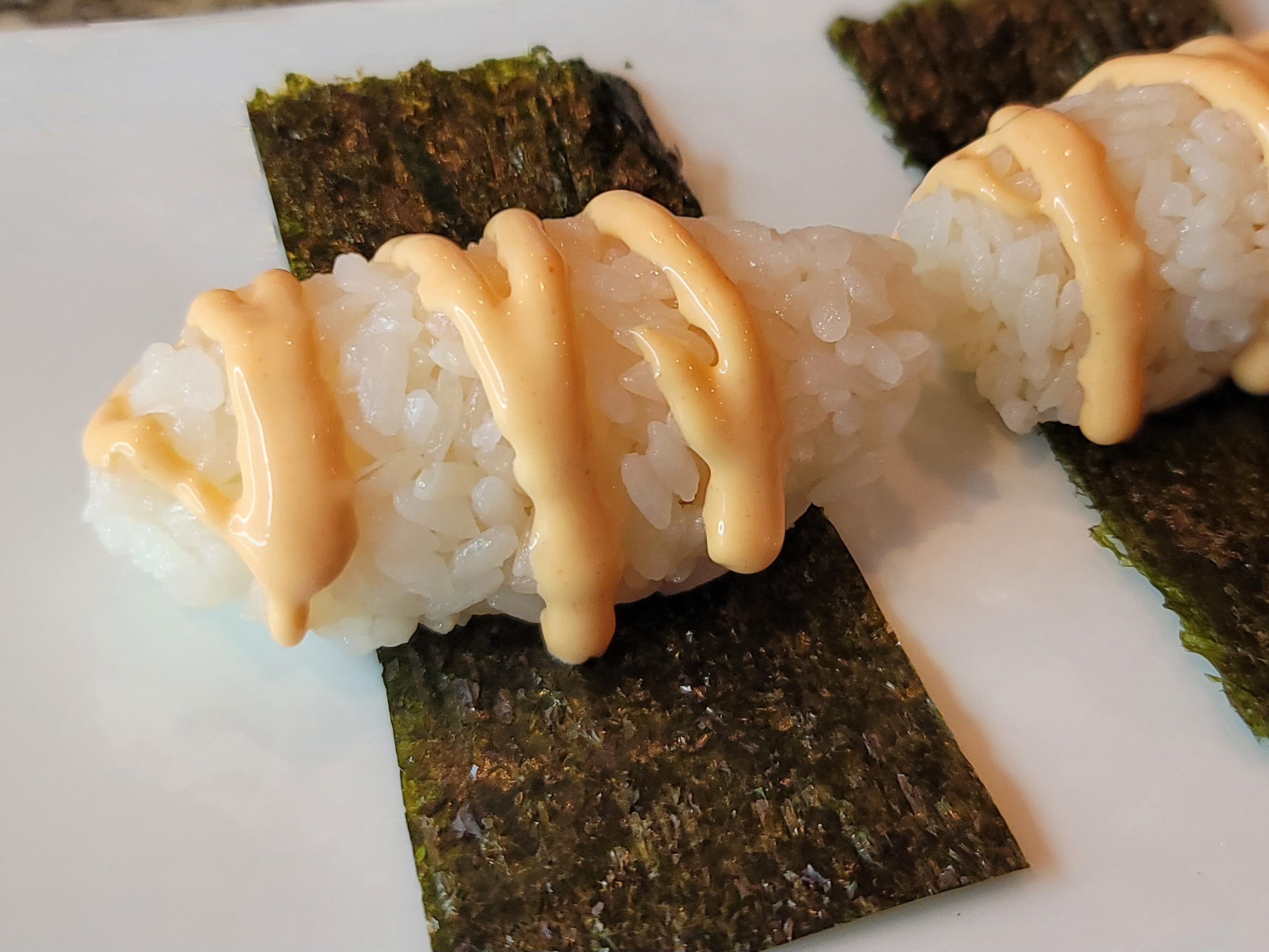 Fluffy sushi rice grains on crispy nori squares with sriracha mayo drizzle and garnish