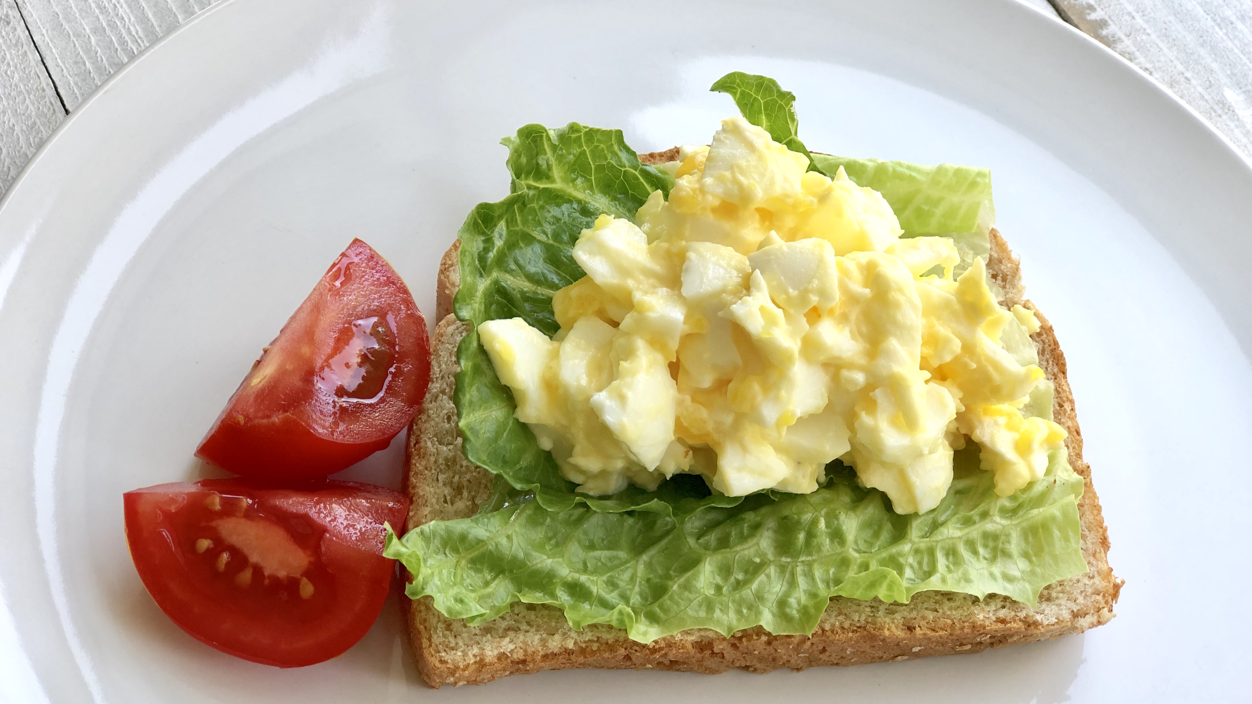 Creamy egg salad with chopped eggs and herbs in a white bowl, ready for sandwich assembly