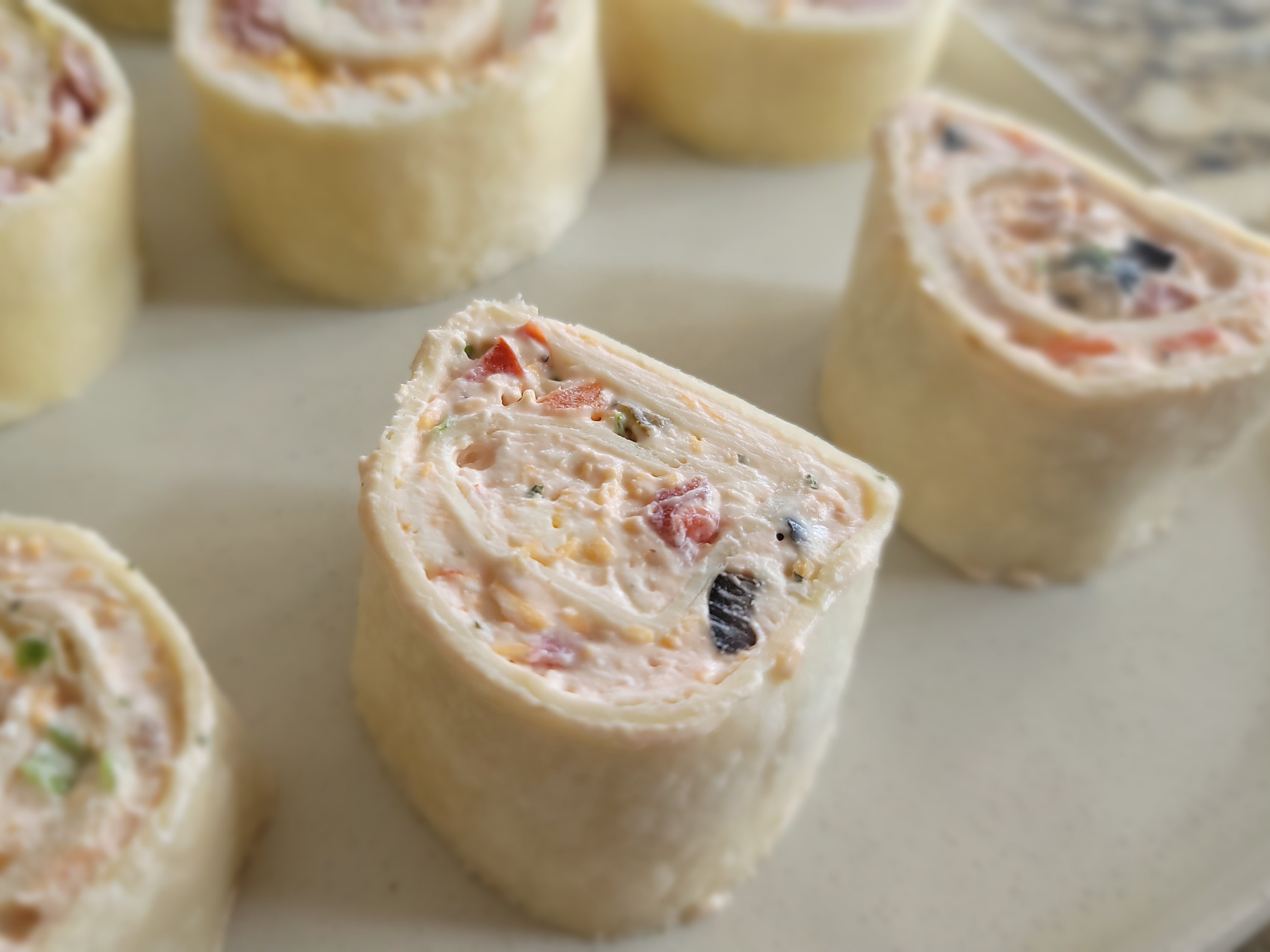 Golden tortilla pinwheels sliced to show spiral filling of cream cheese, green onions, and red peppers on a white serving plate