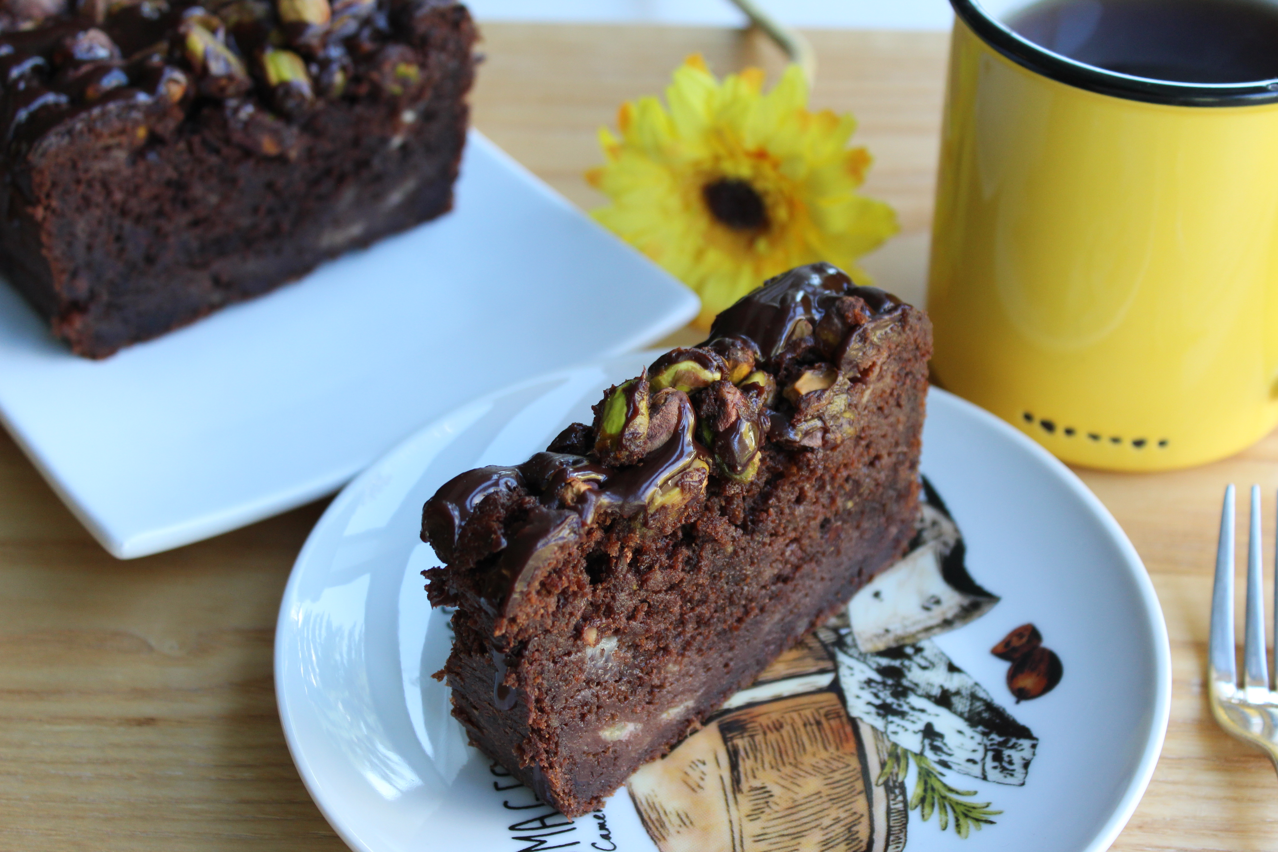Triple chocolate banana bread loaf topped with chocolate ganache and crushed salted pistachios on a light surface